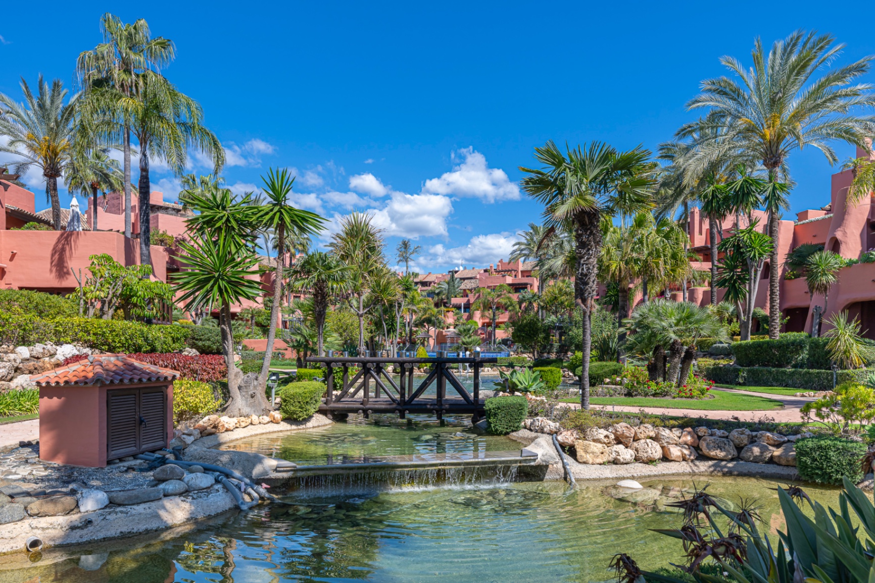 Landscaped gardens and lily pond inside a gated New Golden Mile residential community in Estepona, framed by Andalusian architecture and palms.